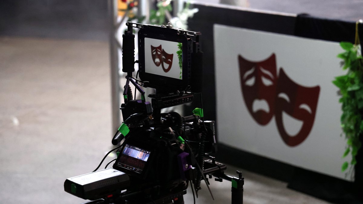 Professional film camera capturing theater performance showing drama and comedy masks.