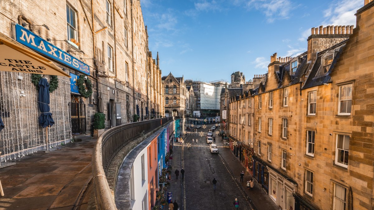 Vibrant view of historic Victoria Street in Edinburgh's Old Town, showcasing colorful shops and cobblestone path under a clear sky.