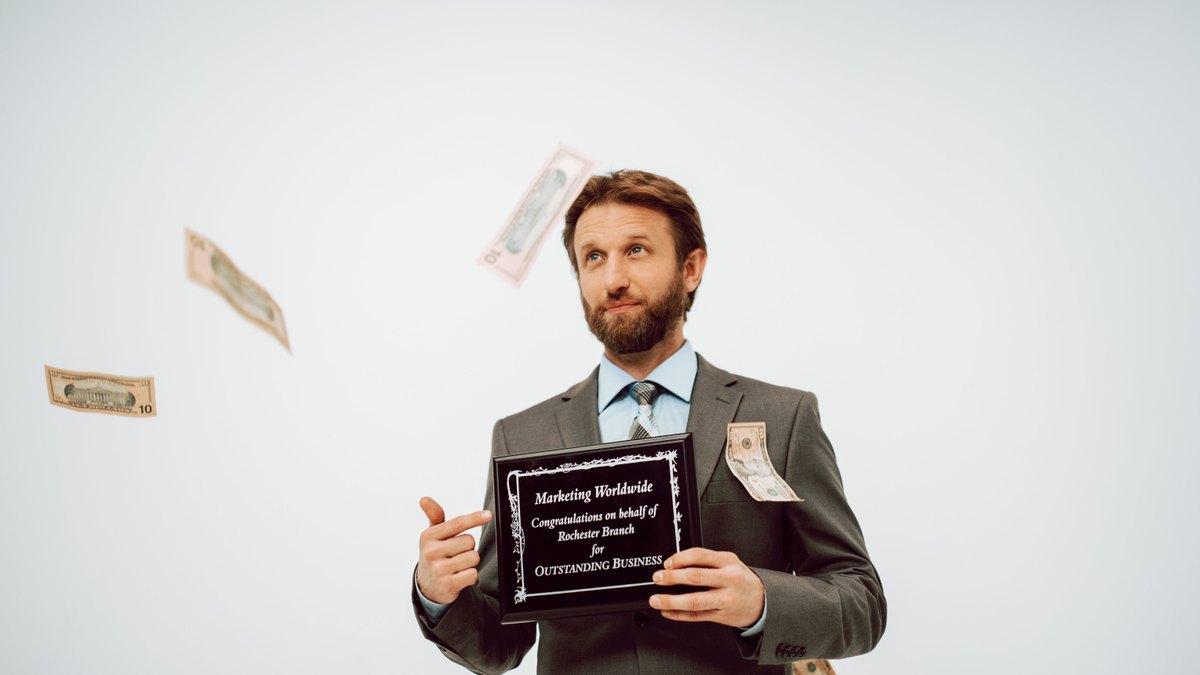 Businessman holding an award plaque, surrounded by falling cash, symbolizing success.