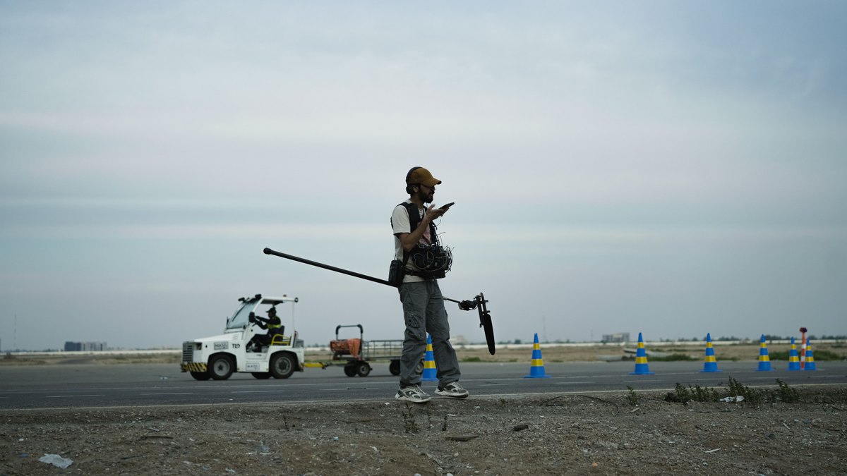 A camera operator checks filming equipment on an empty country road.